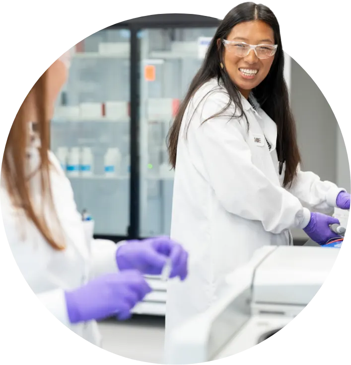 Gray background with blue abstract wave intersecting a circle containing a close-up image of a female employee in the lab